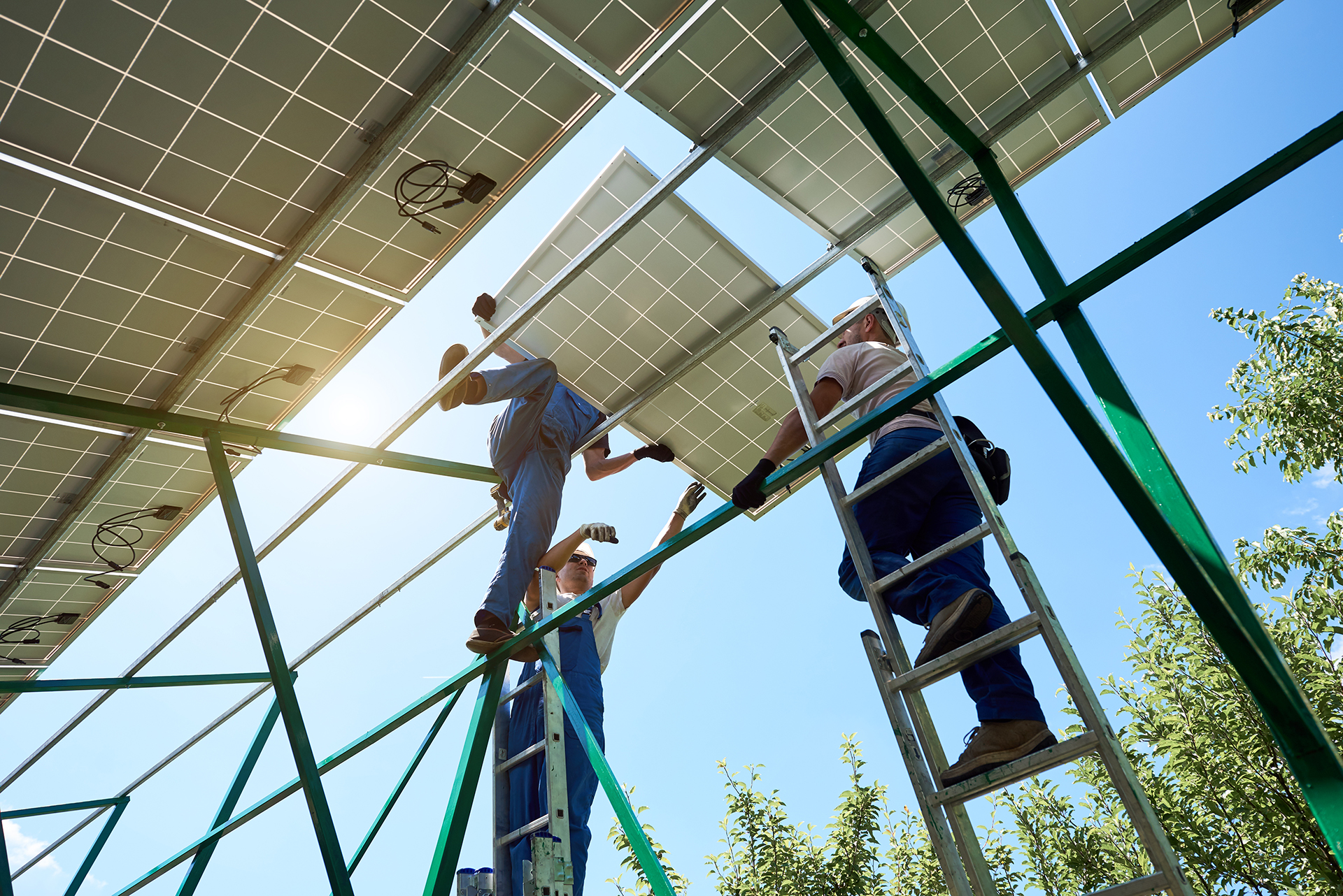professionals installing solar panels on green metallic construction.
